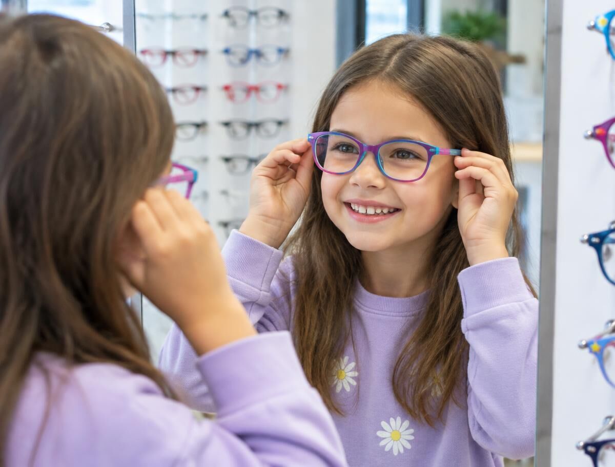 Niña sonriendo frente al espejo mientras se prueba lentes de color (imagen ilustrativa)